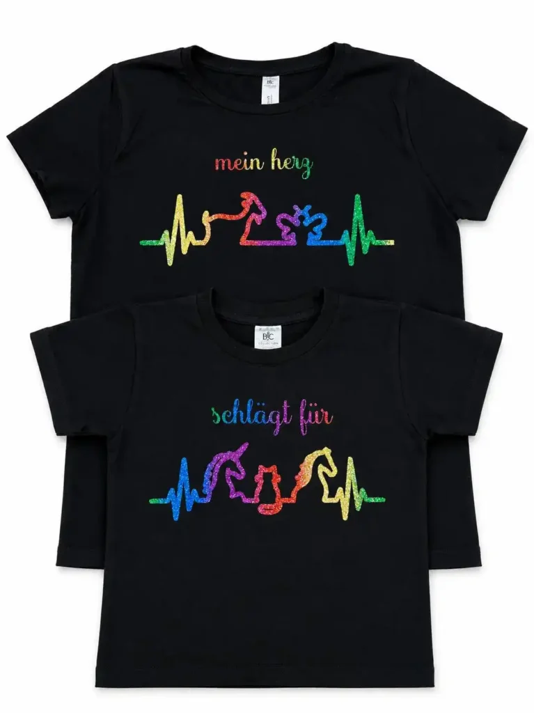 Zwei schwarze Partner-T-Shirts für Erwachsene und Kinder flach übereinander liegend. Auf dem oberen Shirt steht der bunt glitzernde Text "mein herz" über einer regenbogenfarbenen Herzschlag-Linie mit Ziege und Biene. Auf dem unteren Kinder-Shirt steht der Text "schlägt für" über einer EKG-Linie mit einer Einhorn- und Pferde-Silhouette im bunten Glitzer-Look.